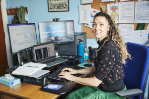 Georgi Daluiso-King, from Sussex MSK Partnership sat at a desk in a doctors office.