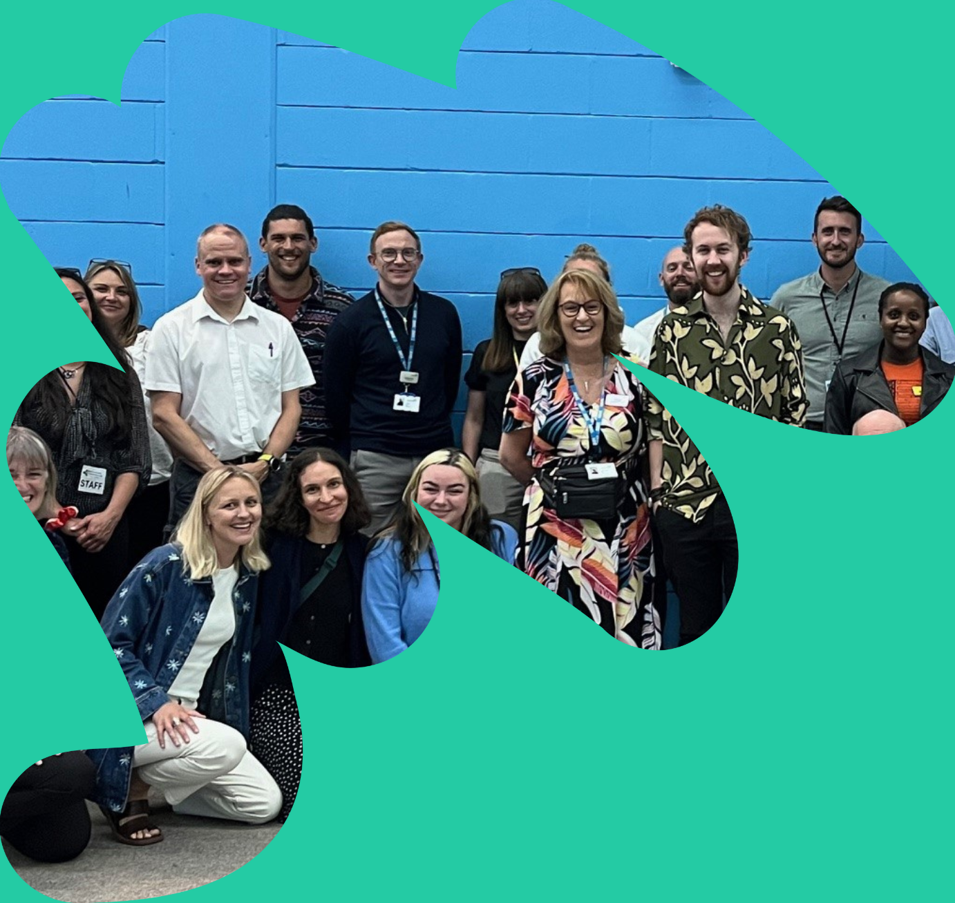 A group of about 30 people stood in a sports hall all facing the camera and smiling