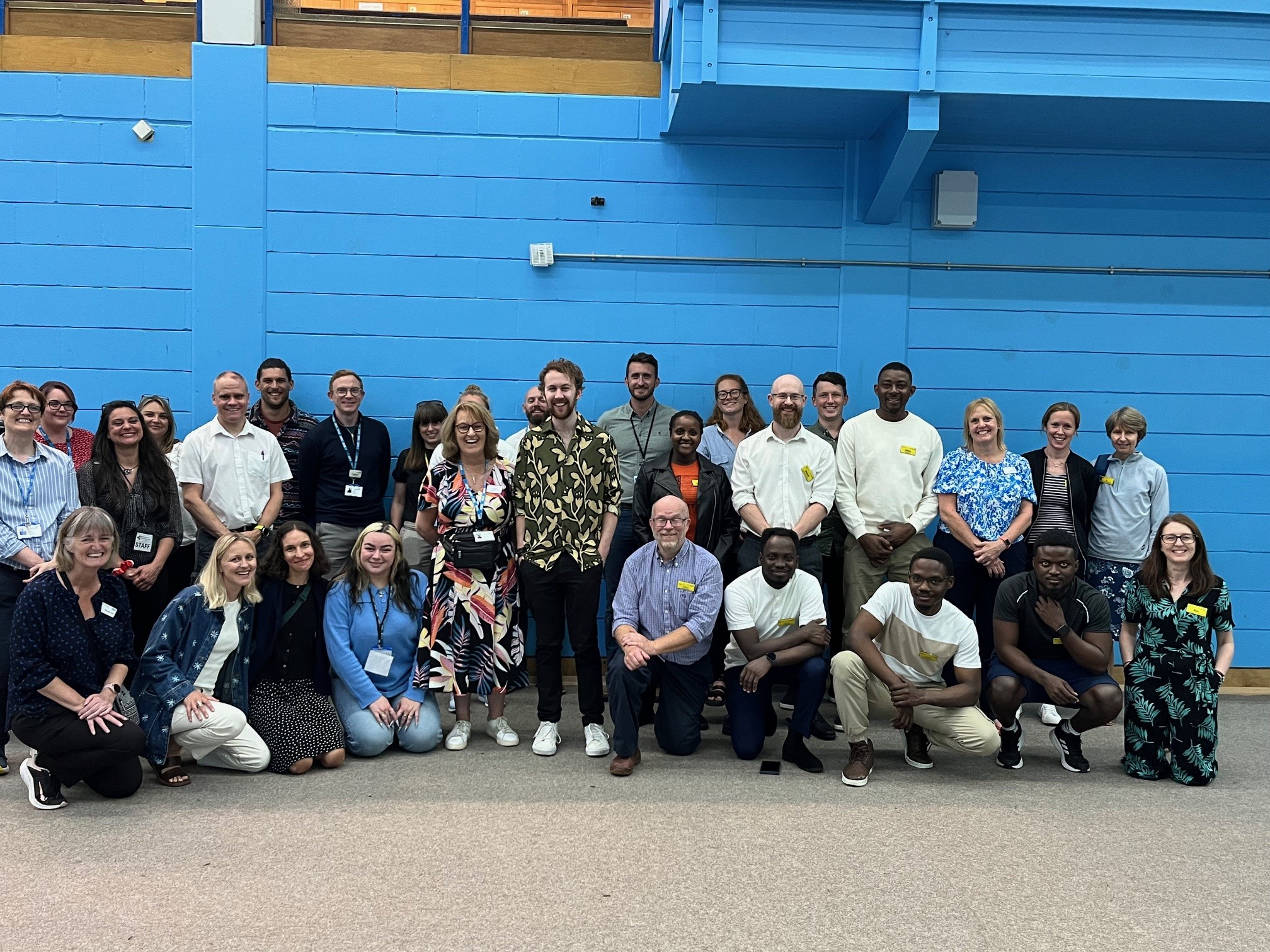 A group of about 30 people stood in a sports hall all facing the camera and smiling
