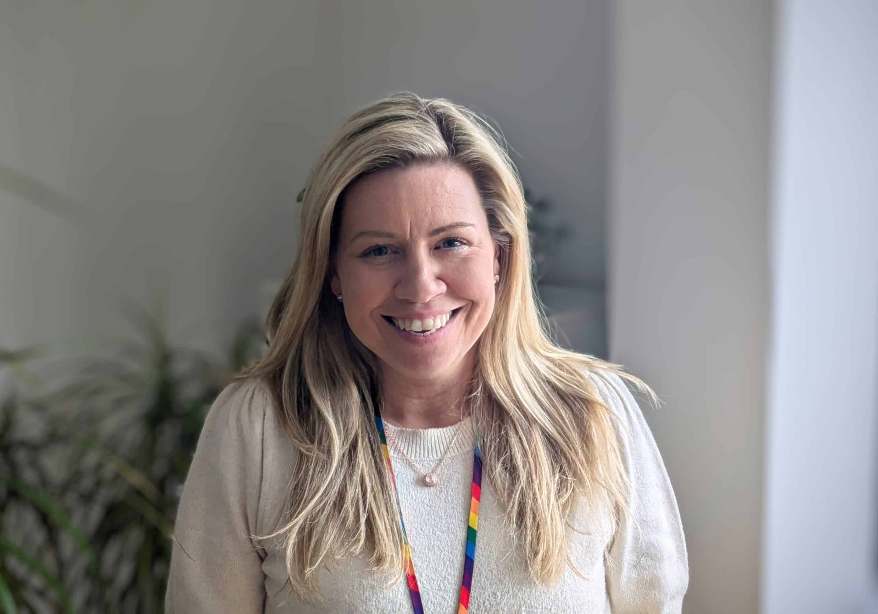 Photo of two white women outside with trees in the background. stood next to each other and smiling towards the camera. The woman on the left has long hair and the woman on the right has a short bobbed hair cut.