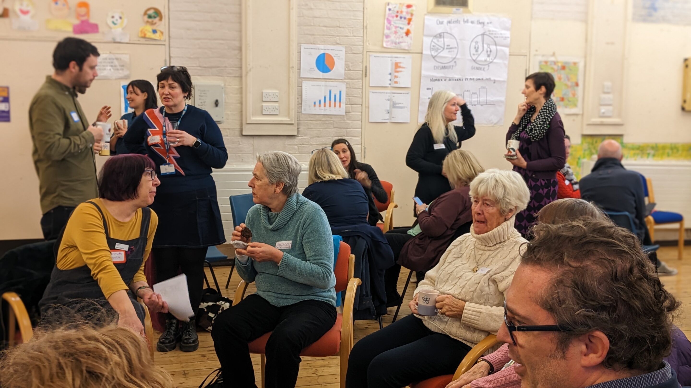 Photo of two white women outside with trees in the background. stood next to each other and smiling towards the camera. The woman on the left has long hair and the woman on the right has a short bobbed hair cut.