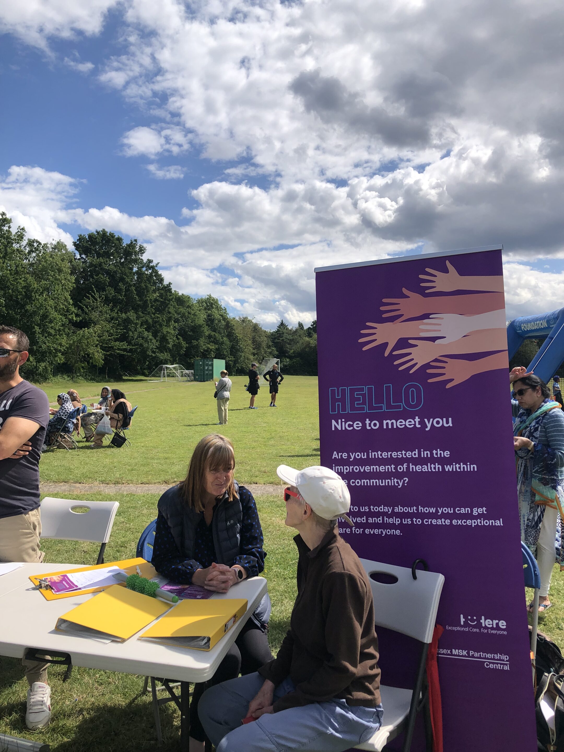 Photo of two white women outside with trees in the background. stood next to each other and smiling towards the camera. The woman on the left has long hair and the woman on the right has a short bobbed hair cut.