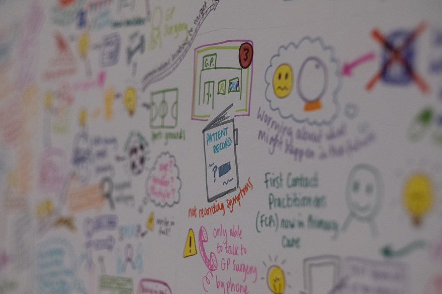 Photo of two white women outside with trees in the background. stood next to each other and smiling towards the camera. The woman on the left has long hair and the woman on the right has a short bobbed hair cut.