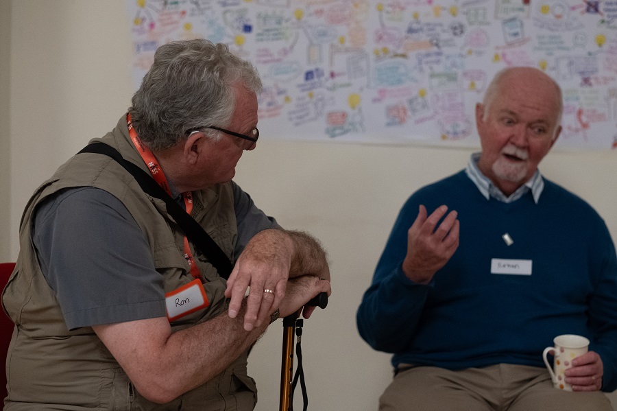 Photo of two white women outside with trees in the background. stood next to each other and smiling towards the camera. The woman on the left has long hair and the woman on the right has a short bobbed hair cut.